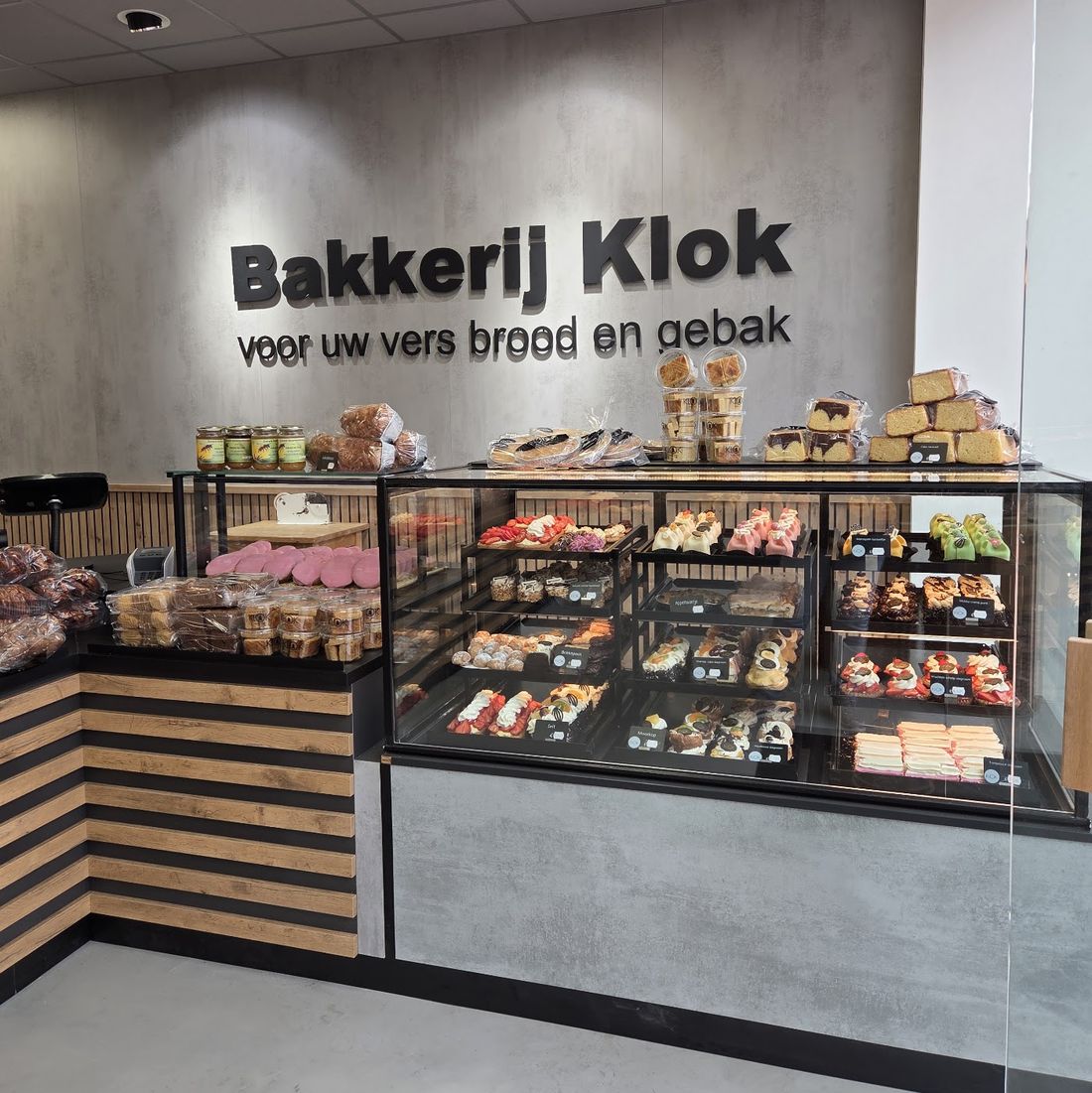 De winkel van Bakkerij Klok: de grijze wand met de naam en de vitrine vol gebak